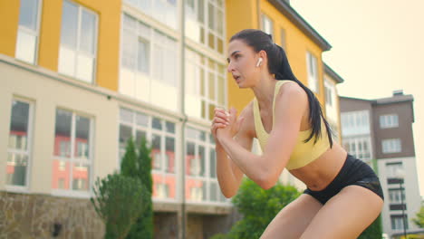 a young female athlete with headphones performs jumping exercises in a city park against the background of buildings. jump on a bench in the park