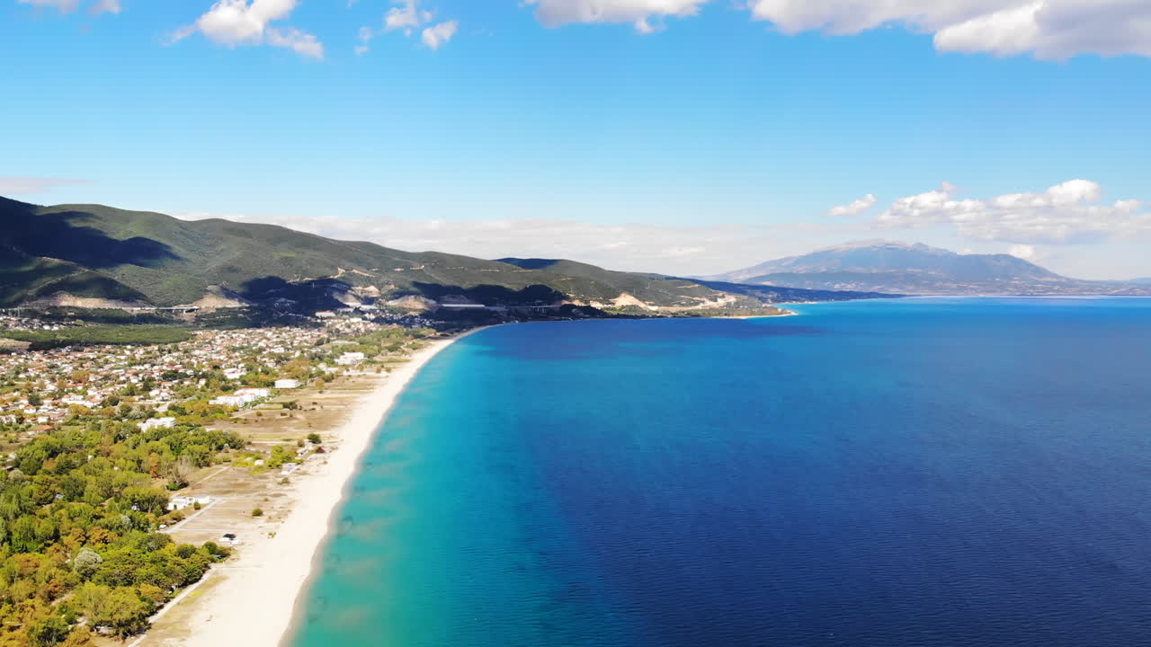 Panorama of the Asprovalta located on the Aegean sea coast with buildings and greenery, green hills. Long beach along the town. Sunny day, view from the drone. Greece