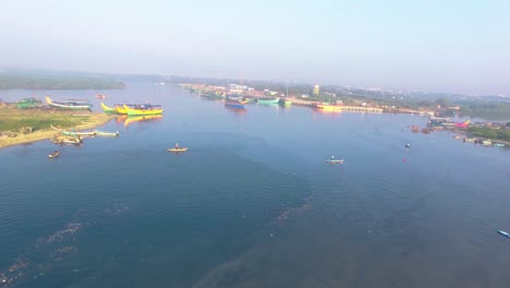 disparo de un dron volando a través de un puerto pesquero que muestra barcos anclados y un pescador pescando con una red