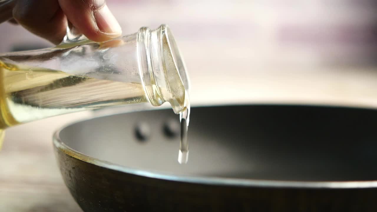 フライパンに油を注ぐ手のクローズアップ