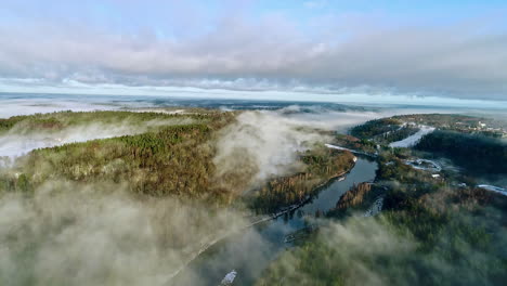 Low valley fog along a river through a picturesque mountain forest - pull back aerial view