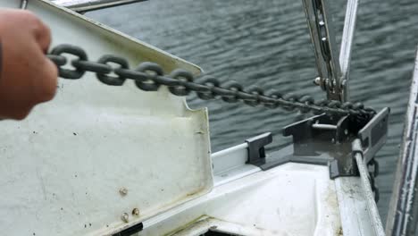 man manually pulling anchor chain on boat from the ocean in alaska