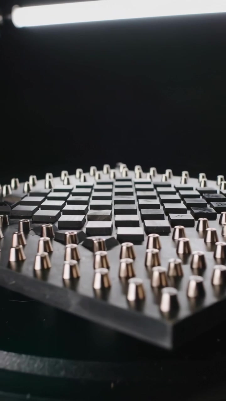 Video verticale: Piattaforma girevole che ruota rivelando piastrelle a scacchiera e perni metallici in uno studio di prodotti.