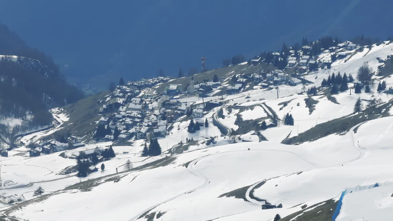 Villaggio innevato di Cheneil, Alpi della Valle d'Aosta, giornata invernale soleggiata, case, chiesa, Italia. Veduta aerea laterale.