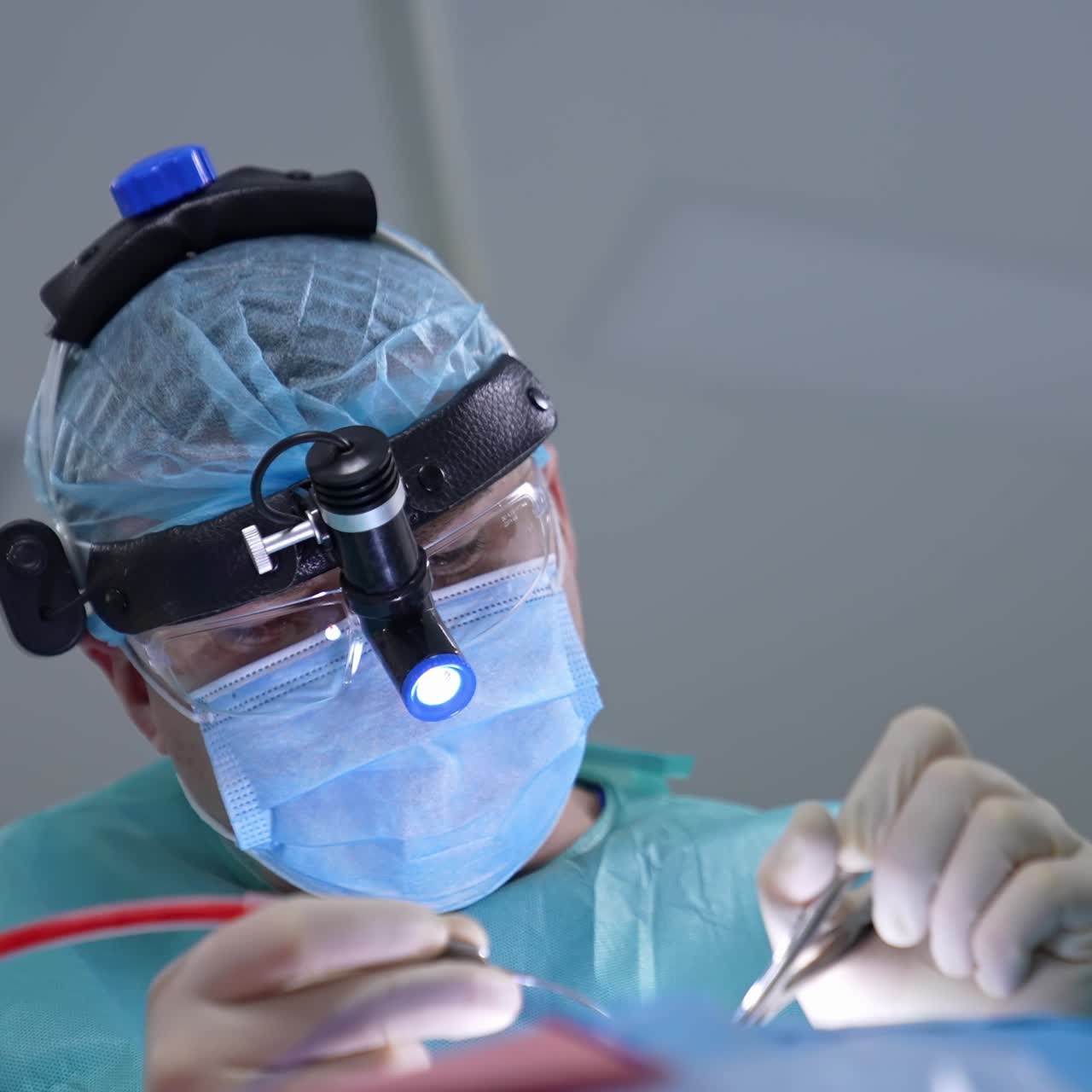 Facial portrait of professional surgeon during operation. Doctor in medical mask and special device on head doing nasal surgery. Nurse assists surgeon in clinic. Close-up