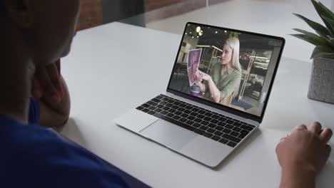 sección media de una mujer afroamericana haciendo una videollamada en una computadora portátil con una colega en la oficina