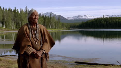 elderly indigenous woman in traditional attire by a serene lake