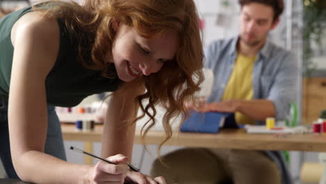 female fashion designer drawing design in foreground as male colleague works on sewing machine