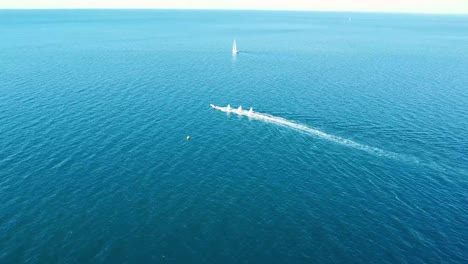 motorboat tows sailboats on calm clear blue sea