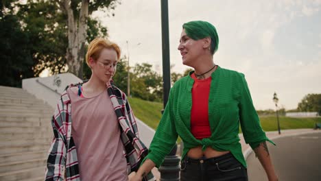 Two-lesbian-girls-with-short-haircuts-of-bright-colors-in-plaid-shirts-spin-around-a-lamppost-during-their-date-and-then-hold-hands-and-walk-along-the-street-talking