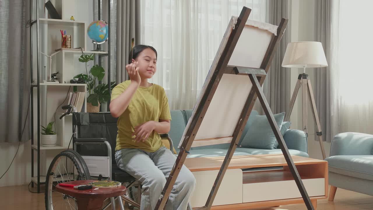 Asian Artist Girl In Wheelchair Holding Paintbrush Wipe The Sweat Before Crossing His Arms And Smiling After Finish Painting On The Canvas