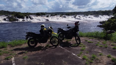 an aerial shot that begins with a slight downward tilt, focusing on the two motorcycles, and then ascends in an upward tilt to reveal the majestic caroní river