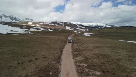 flyover of camper van driving on dirt road in open plateau, montenegro