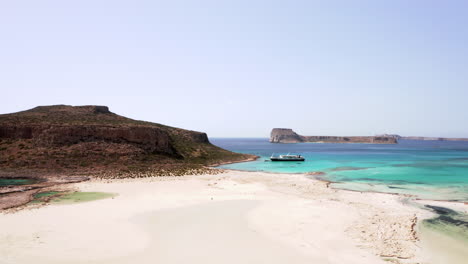 Luftaufnahme-Des-Balos-Strands-Im-Norden-Kretas-An-Einem-Schönen-Sonnigen-Tag-Mit-Türkisfarbenem-Wasser-–-Weißer-Sand-Mit-Strandgängern-Im-Vordergrund