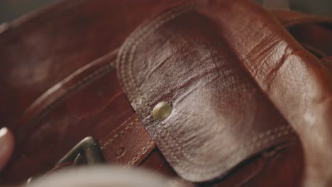 female hand gently wiping the surface of outside pocket of a brown leather bag with a wet white rounded sponge - closeup shot