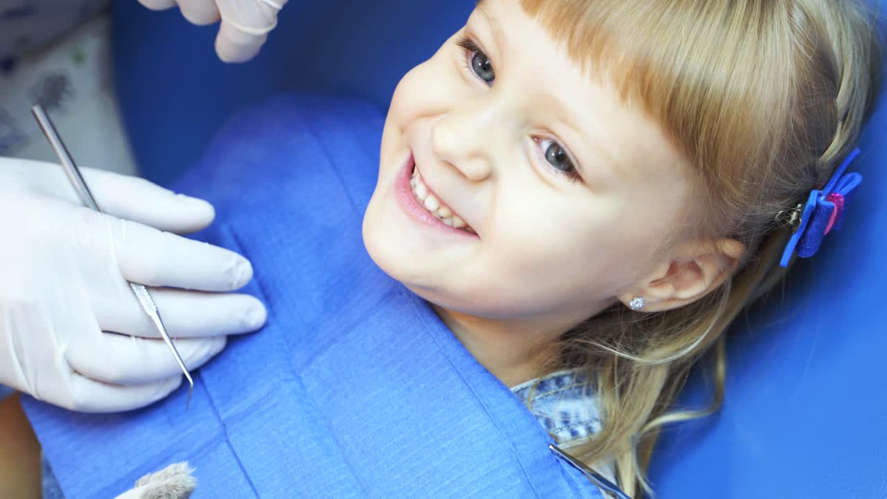 little girl in a blue chair at the dentist shows teeth for treatment
