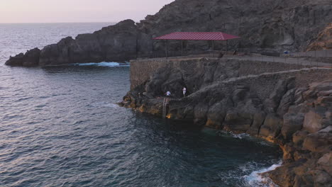 young guys fishing from a stone cliff on a sea shore during sunset