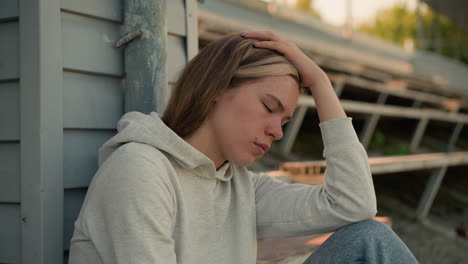 close-up of young lady resting her head on hand, appearing asleep, with warm sunlight casting gentle glow, background features blurred trees and pole