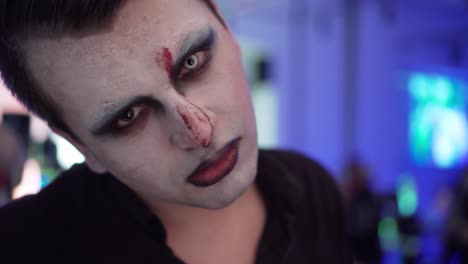 man with face paint showing tongue and party in background, closeup portrait