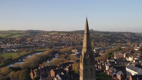 aerial focused on church steeple in a countryside uk town. sunset light hits the side of the church for dramatic effect