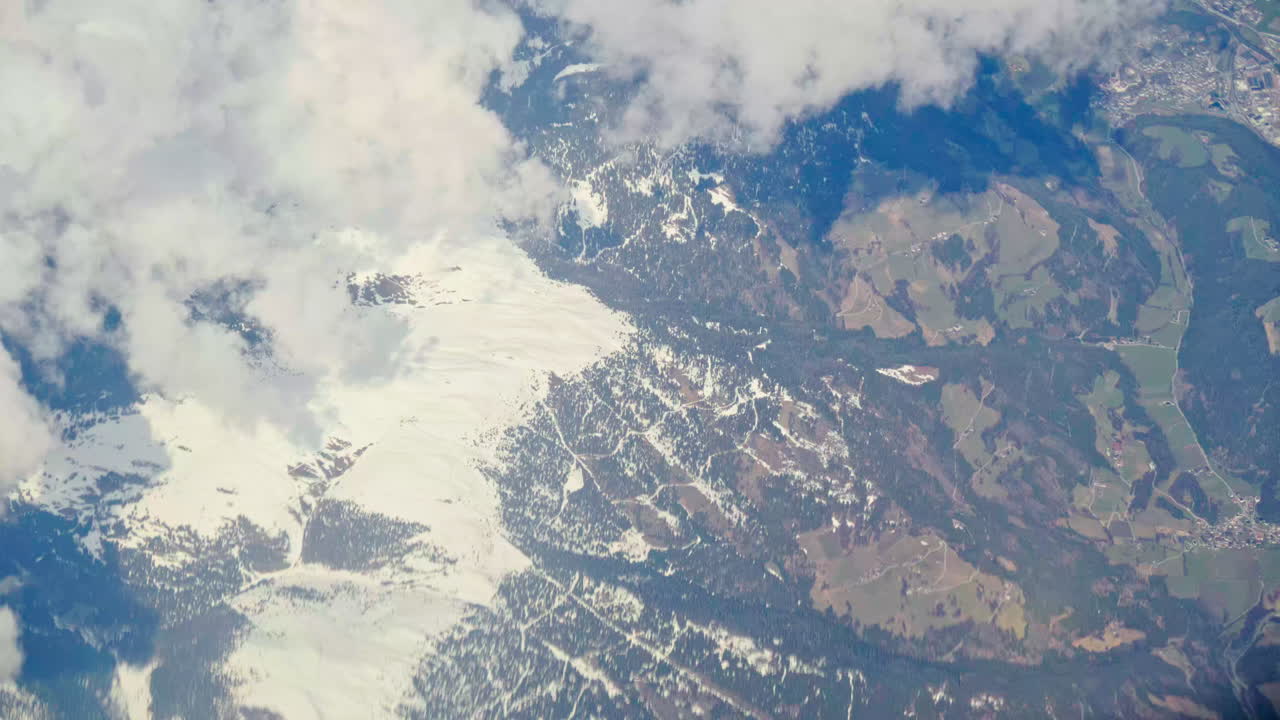 Aerial view of white, fluffy clouds above snowy mountains seen from an airplane window