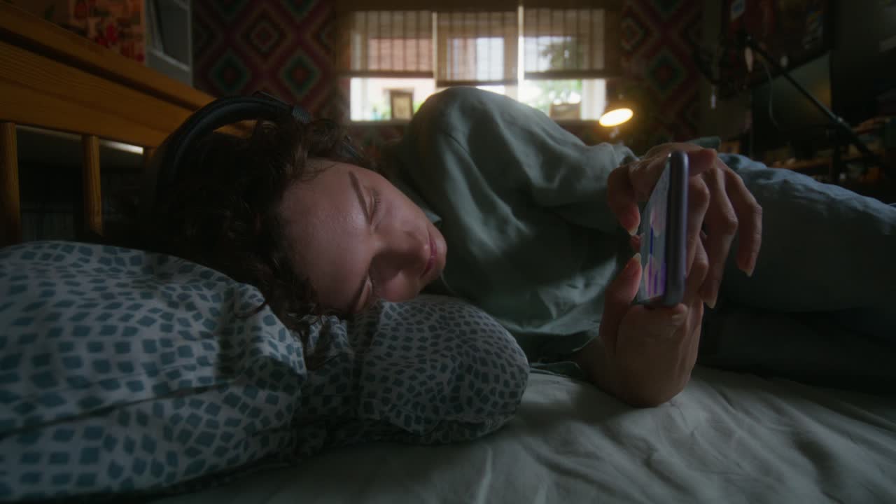 헤드폰과 전화로 침대에서 휴식을 취하는 여자