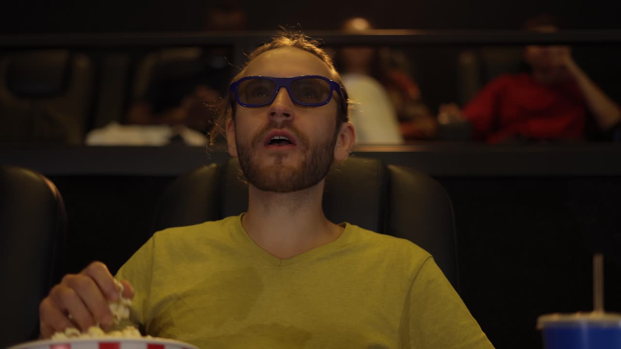 A man in 3d glasses watching movie at the cinema and taking popcorn