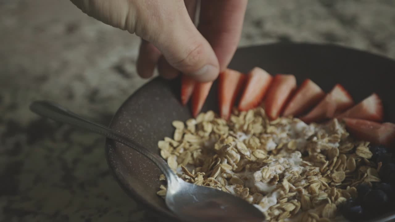 mano colocando una rebanada fresca de fresa en un plato de cereales