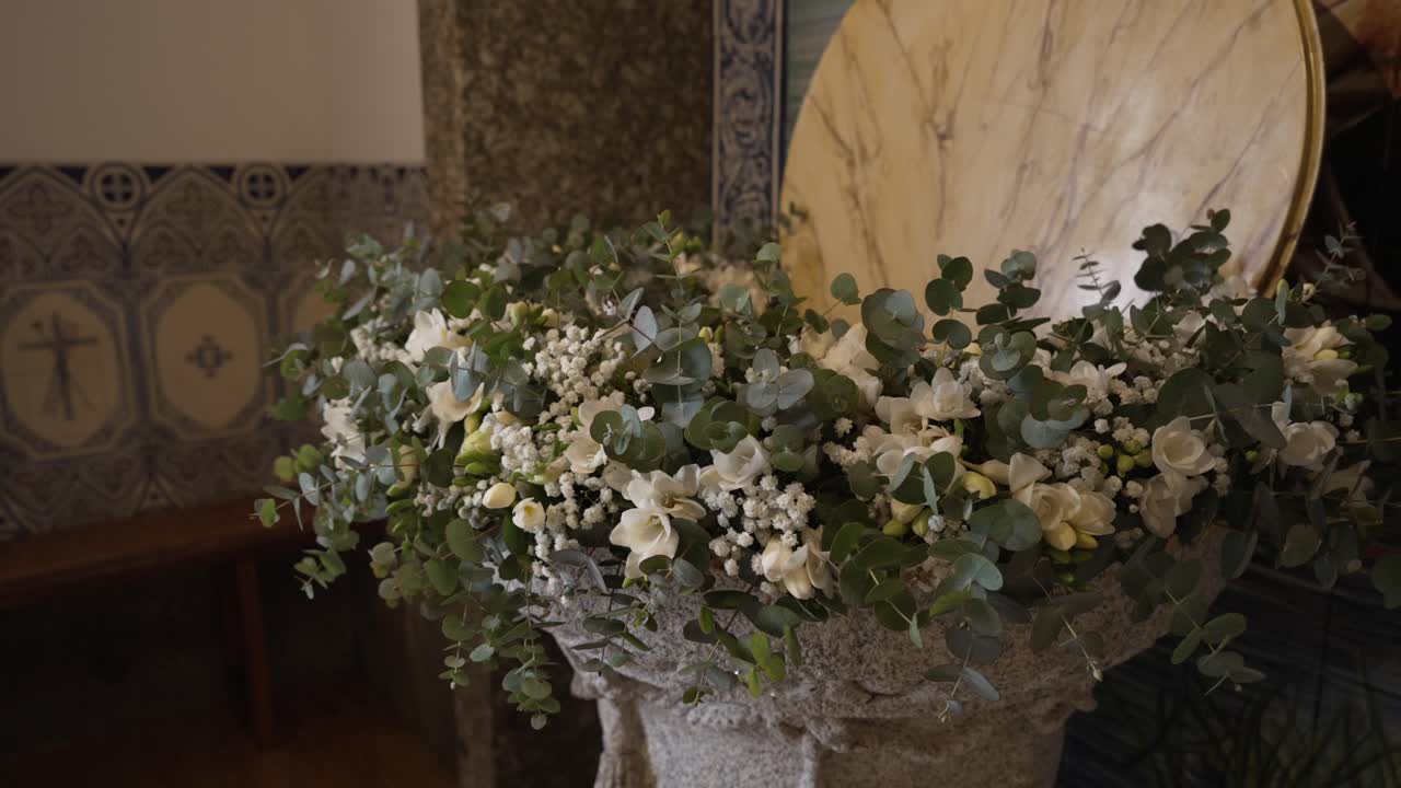 Baptismal font overflowing with white roses baby's breath and eucalyptus leaves in a church