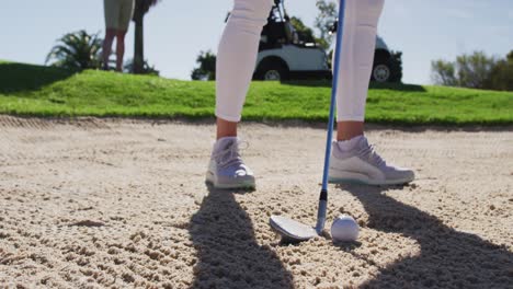 dos mujeres caucásicas jugando al golf una disparando desde el búnker