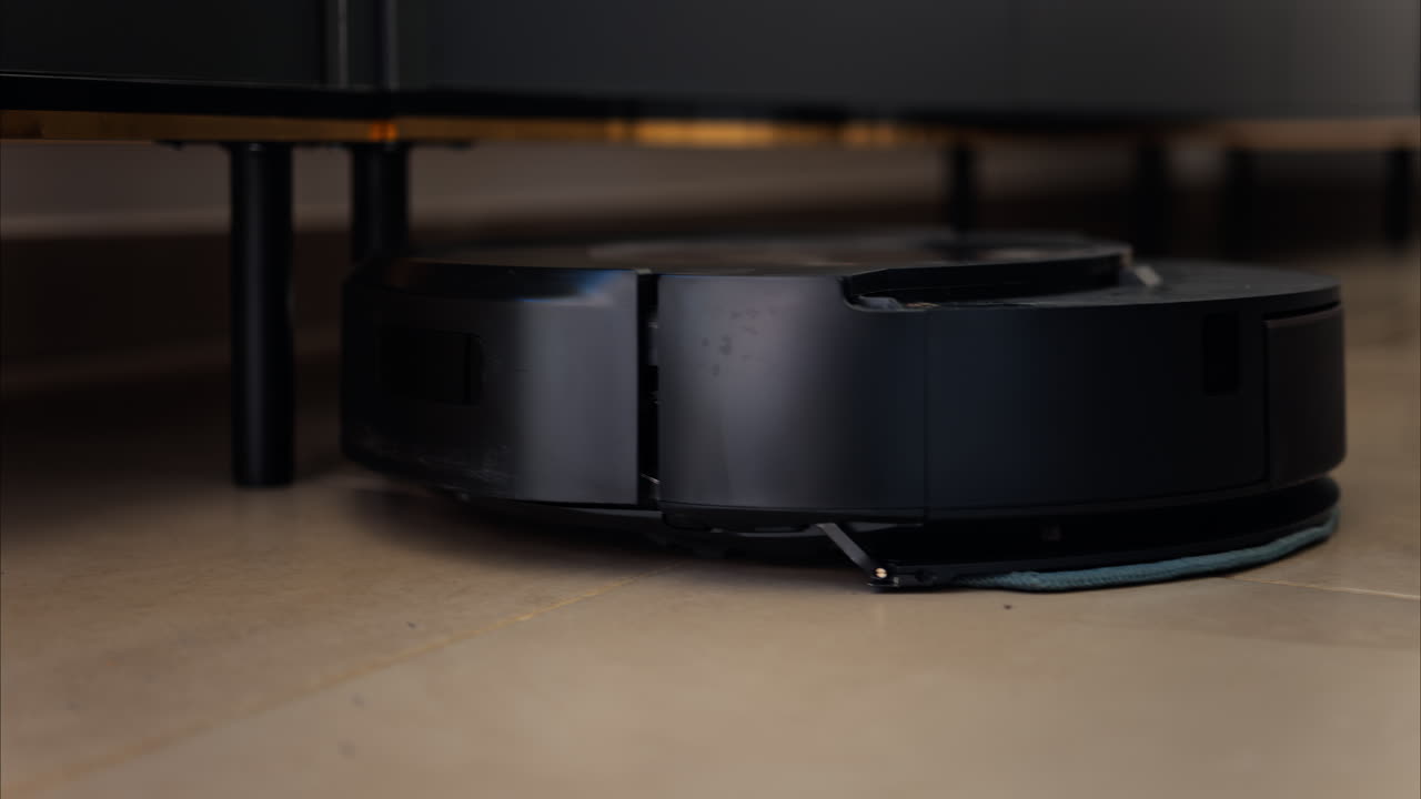 Close up of a black robot vacuum cleaner moving and rotating on the floor tiles