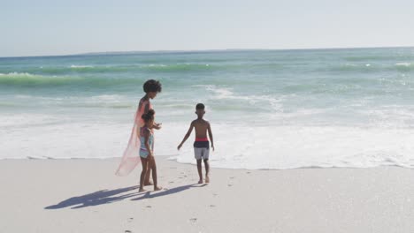 Madre-Afroamericana-Sonriente-Con-Niños-Vistiendo-Trajes-De-Baño-En-La-Playa-Soleada