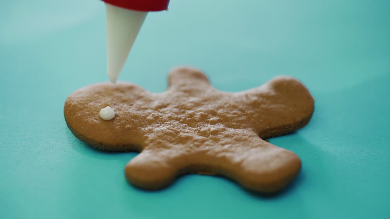 confectioner is painting cookies in the form of a ginger man on the New Year on the table in the kitchen. The process of decorating by glaze. Close-up