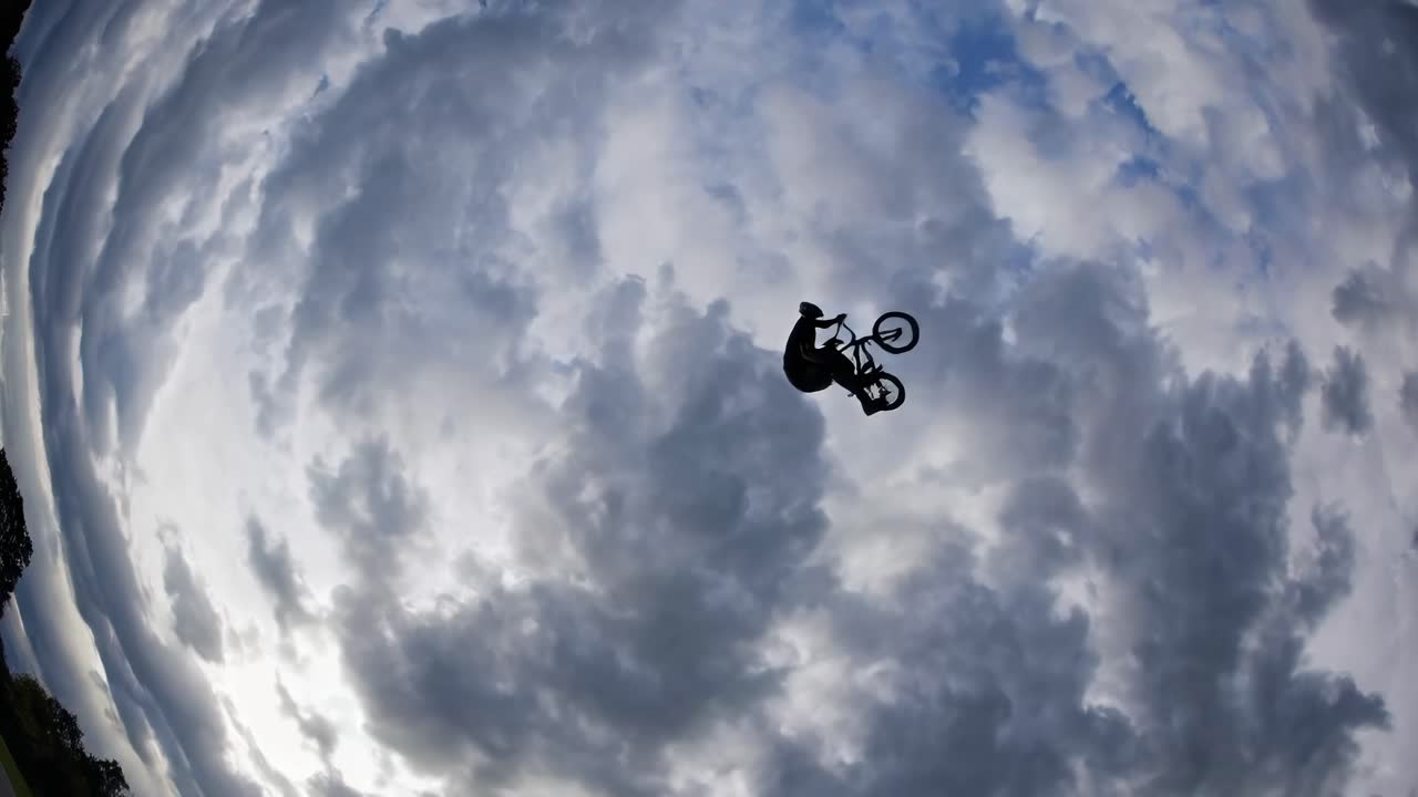 Silhouette of a cyclist mid-air against dramatic clouds, captured from a low-angle
