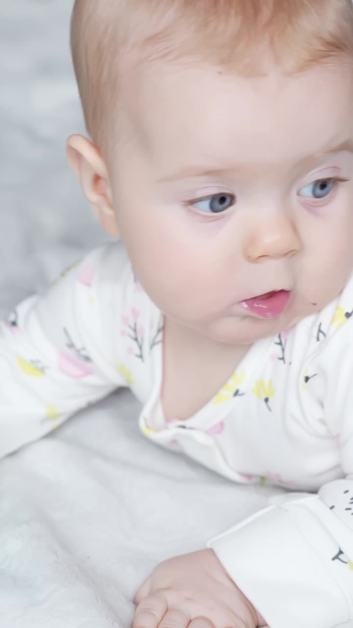 Vertical - Baby Girl With Bright Blue Eyes In White Onesie, Chews On Soft Mint-green Teething Toy. closeup shot
