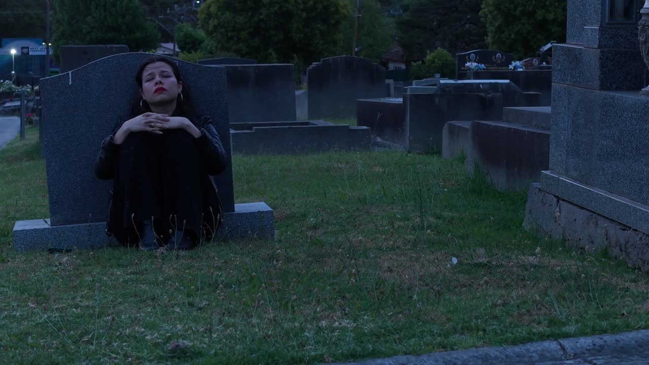 Una ragazza in pensierosa solitudine in un cimitero al crepuscolo a Melbourne. L'illuminazione suggestiva e l'ambiente sereno creano un'atmosfera contemplativa, evidenziando emozioni profonde.