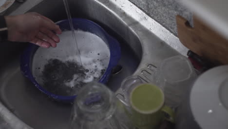 washing dishware under running tap water from the faucet of kitchen sink