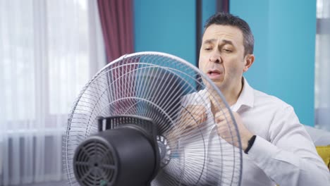 overwhelmed by the heat, the man turns on the fan and relaxes.