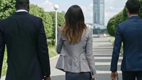 Businessmen-And-Businesswoman-Wearing-Elegant-Suits-Talking-And-Holding-Briefcases-While-They-Walking-In-The-Park