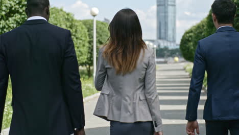우아한 정장을 입은 기업인과 여성 사업가가 공원을 걷는 동안 이야기하고 서류 가방을 들고 있습니다.