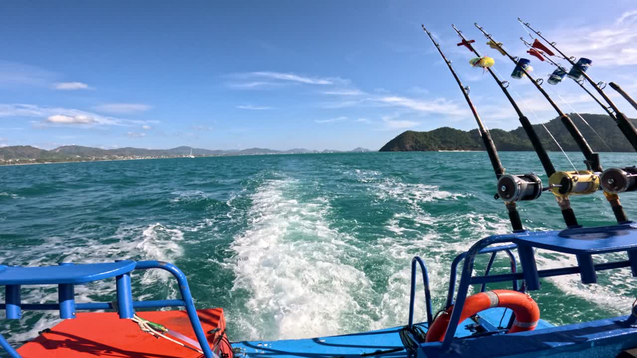 A vibrant fishing boat navigates clear waters near Phuket, showcasing fishing rods and scenic ocean views under bright daylight