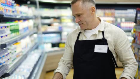 Un-Trabajador-De-Una-Tienda-De-Abarrotes-De-Mediana-Edad-Trae-Productos-En-Una-Caja-Y-Los-Coloca-En-Los-Estantes.-Trabajar-En-La-Tienda.-Felicidad