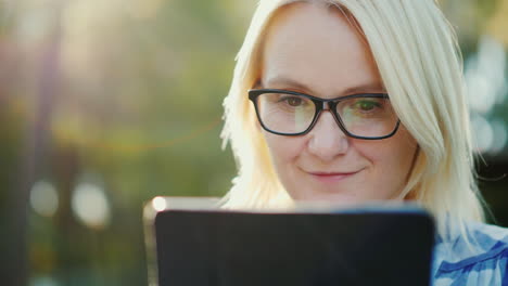 portrait of a young woman wearing glasses enjoying a tablet in the park beautiful sun glare 4k slow