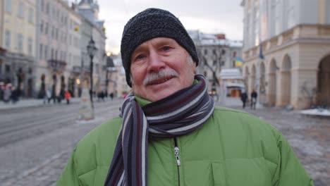 Portrait-of-old-senior-man-tourist-smiling,-looking-at-camera-in-winter-city-center-of-Lviv,-Ukraine