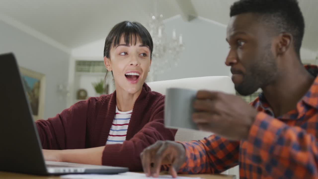 pareja feliz y diversa sentada a la mesa y trabajando con una computadora portátil