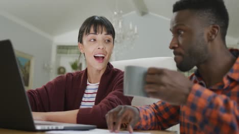 happy diverse couple sitting at table and working with laptop