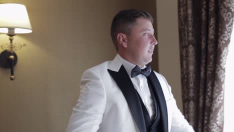 handsome stylish groom man wearing white jacket at home in living room, slow motion indoors portrait