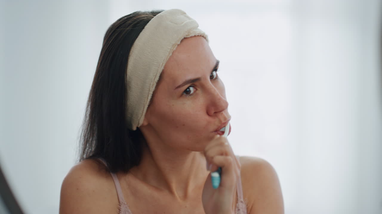 Brushing teeth girl morning at bathroom mirror. Diligent woman massaging gums