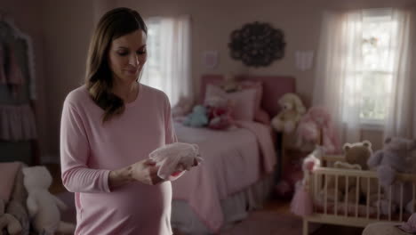 pregnant woman in baby nursery holding baby clothes