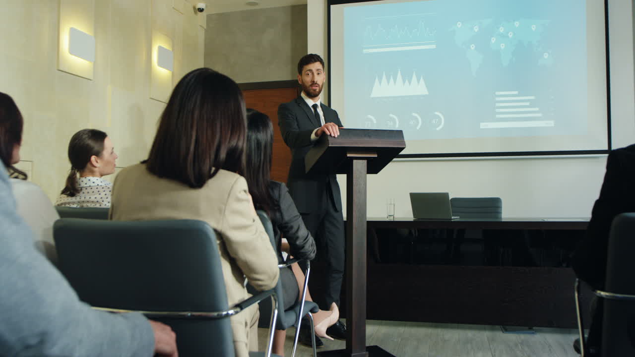 alejar la cámara sobre un hombre de negocios caucásico hablando en un podio en una sala de conferencias y mostrando algunos gráficos y gráficos en la pantalla grande